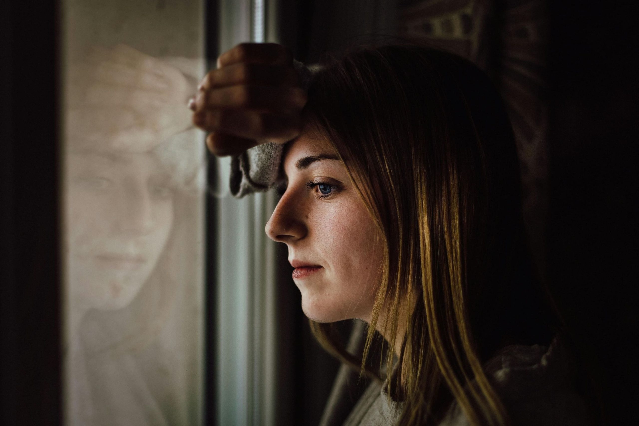 Vrouw die in stilte naar buiten kijkt en luistert naar haar innerlijke stem in een moment van rust.